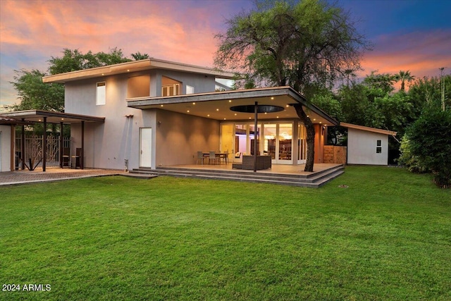 back house at dusk featuring a yard and a patio area