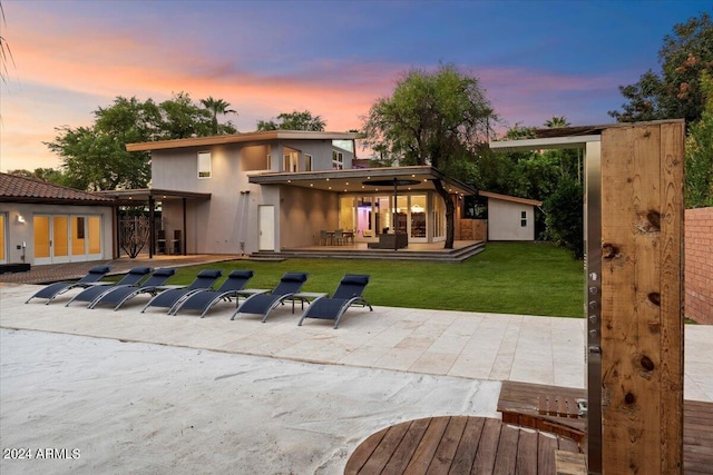 back house at dusk featuring a yard, a storage unit, and a patio area