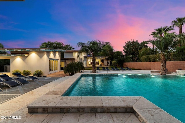 pool at dusk with pool water feature and a patio area