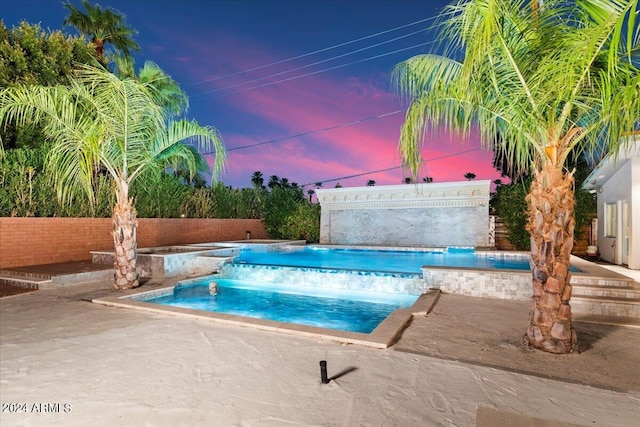 pool at dusk with a hot tub and a patio