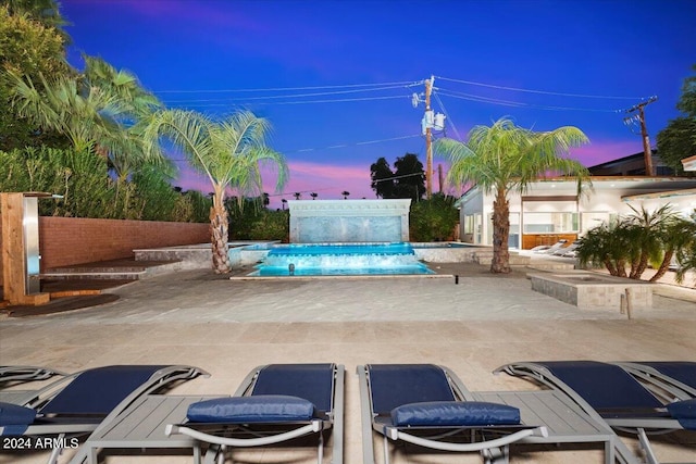 pool at dusk featuring a hot tub, pool water feature, and a patio area