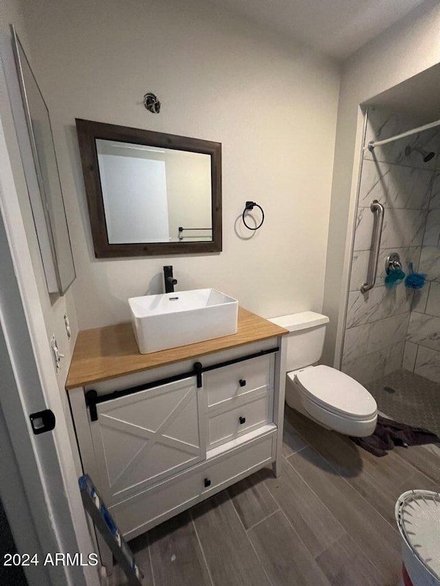 bathroom featuring hardwood / wood-style floors, vanity, toilet, and tiled shower