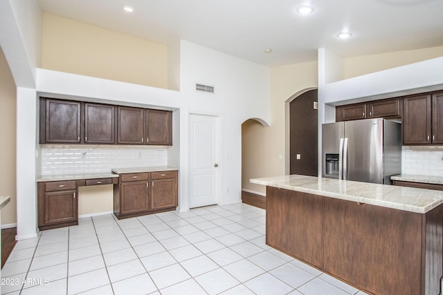 kitchen featuring light stone counters, light tile patterned flooring, backsplash, stainless steel fridge with ice dispenser, and dark brown cabinetry