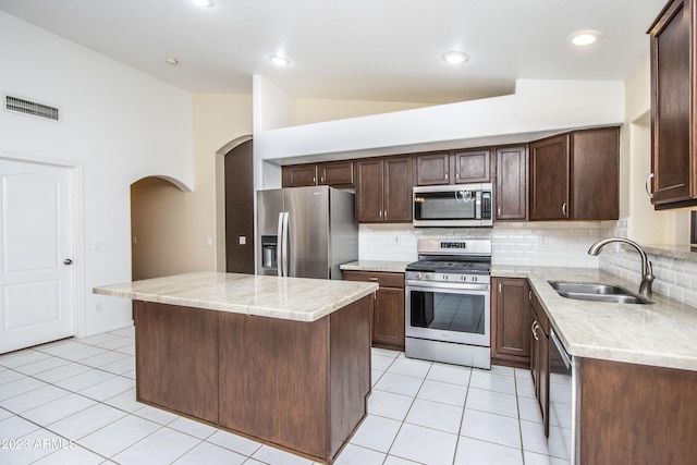 kitchen with vaulted ceiling, decorative backsplash, a kitchen island, appliances with stainless steel finishes, and sink