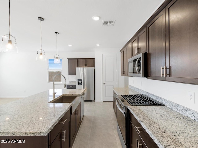 kitchen with a sink, visible vents, dark brown cabinetry, light stone counters, and appliances with stainless steel finishes