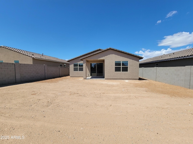 rear view of house with a tile roof, a fenced backyard, and stucco siding