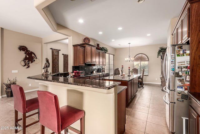 kitchen featuring kitchen peninsula, dark stone countertops, a breakfast bar, and stainless steel refrigerator