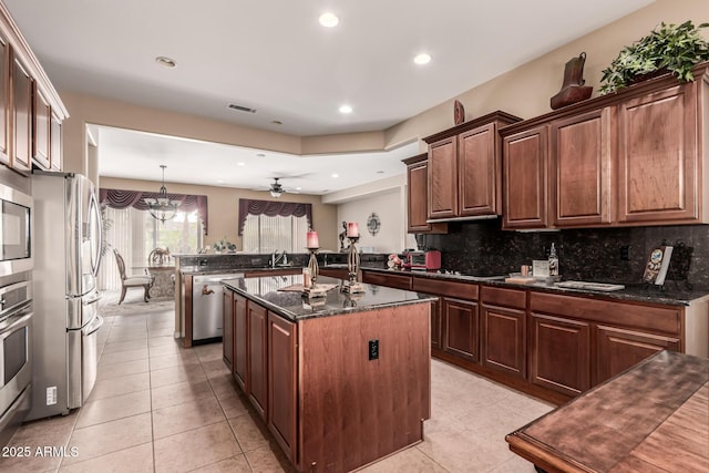 kitchen featuring decorative light fixtures, appliances with stainless steel finishes, a kitchen island with sink, and dark stone counters