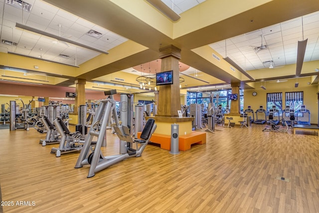 exercise room with a high ceiling, a paneled ceiling, and light wood-type flooring