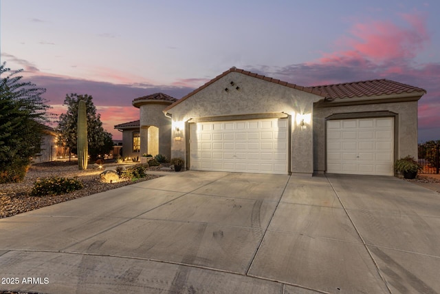 mediterranean / spanish home with a tile roof, stucco siding, an attached garage, and concrete driveway