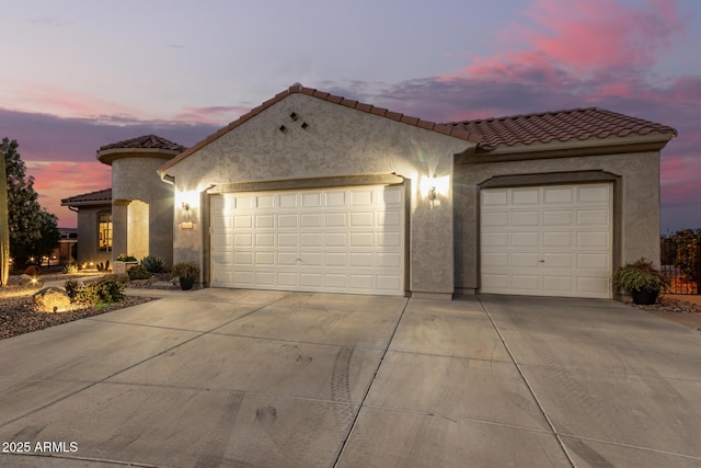 mediterranean / spanish-style house with a tile roof, a garage, driveway, and stucco siding