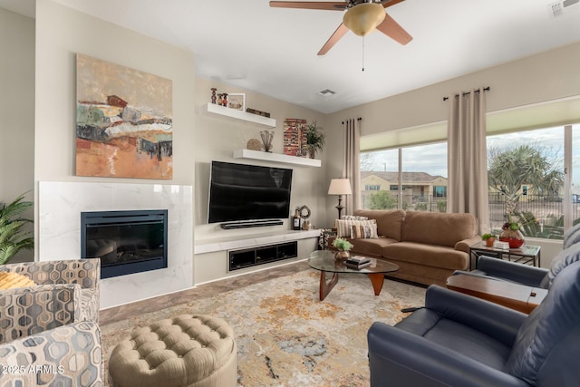 living area featuring visible vents, a premium fireplace, and a ceiling fan