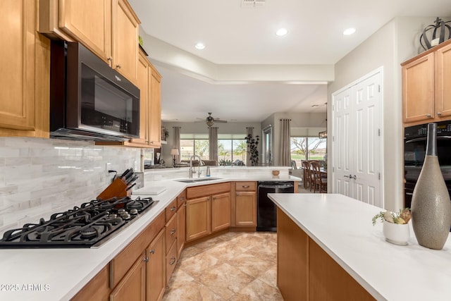 kitchen featuring backsplash, light countertops, a peninsula, black appliances, and a sink