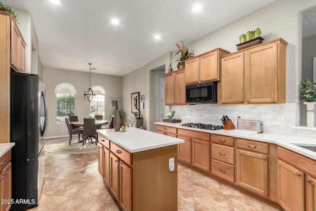 kitchen featuring decorative backsplash, black appliances, light countertops, and a center island