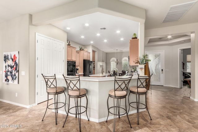 kitchen with light brown cabinetry, visible vents, stainless steel fridge, and a kitchen bar