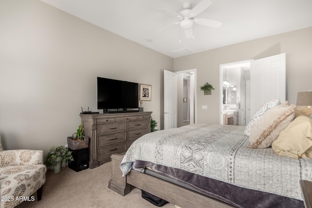 bedroom featuring light carpet, ensuite bathroom, and a ceiling fan