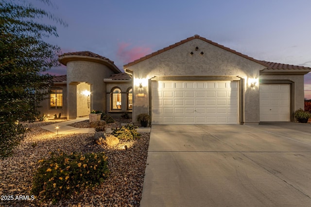 mediterranean / spanish house with stucco siding, concrete driveway, an attached garage, and a tile roof