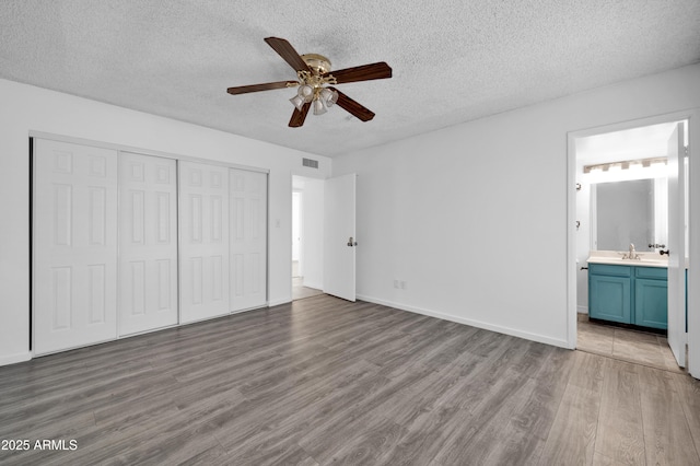 unfurnished bedroom featuring ensuite bathroom, ceiling fan, sink, wood-type flooring, and a closet