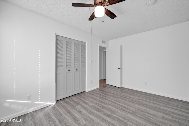 unfurnished bedroom featuring a textured ceiling, ceiling fan, light hardwood / wood-style flooring, and a closet