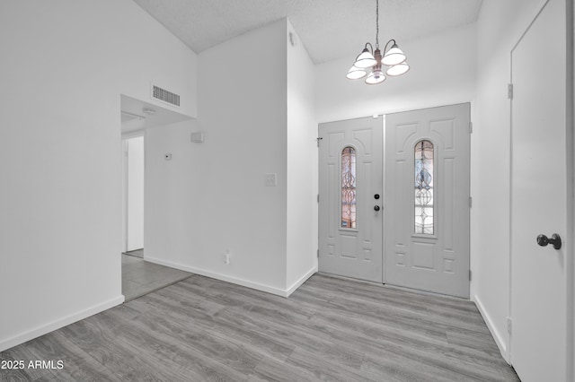 entryway with a chandelier, a textured ceiling, light hardwood / wood-style floors, and high vaulted ceiling