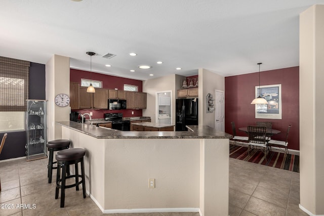 kitchen with a kitchen island with sink, black appliances, hanging light fixtures, light tile patterned floors, and a breakfast bar area