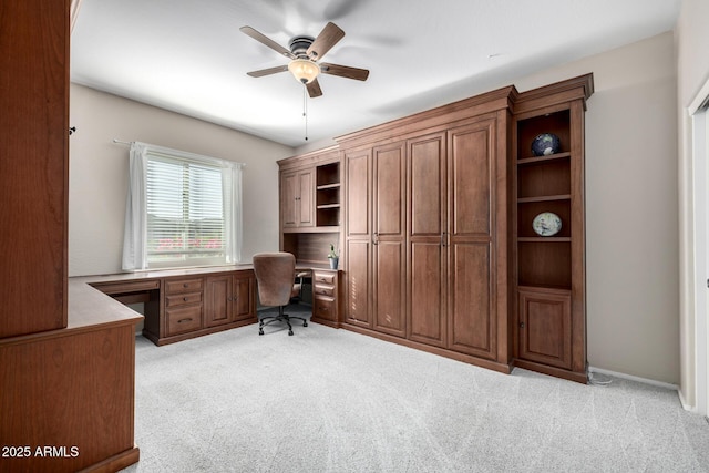 unfurnished office featuring ceiling fan, built in desk, and light carpet