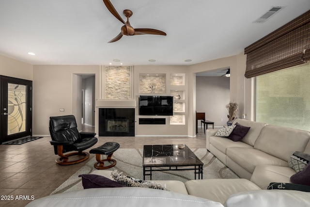 living room featuring a tiled fireplace, ceiling fan, and built in features