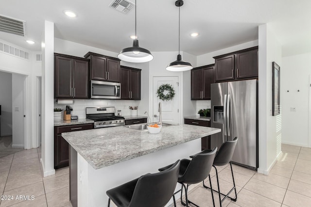 kitchen with pendant lighting, sink, an island with sink, light tile patterned flooring, and stainless steel appliances