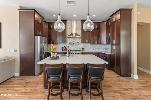 kitchen with light wood finished floors, visible vents, appliances with stainless steel finishes, wall chimney exhaust hood, and a sink