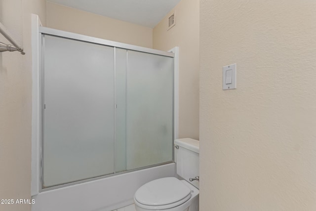 bathroom featuring combined bath / shower with glass door and toilet