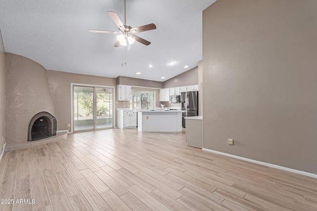 unfurnished living room with ceiling fan, lofted ceiling, a fireplace, and light wood-type flooring