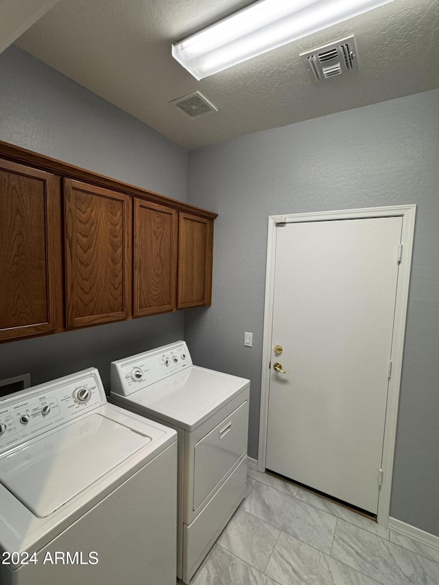 clothes washing area with cabinets, separate washer and dryer, and a textured ceiling