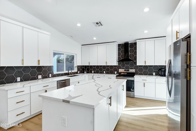 kitchen featuring white cabinets, appliances with stainless steel finishes, a kitchen island, and wall chimney exhaust hood