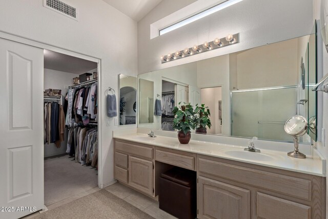 bathroom featuring double vanity, a stall shower, a walk in closet, tile patterned flooring, and vaulted ceiling