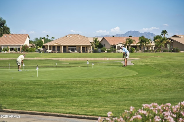 view of community with view of golf course, an area to practice putting, a yard, and a mountain view