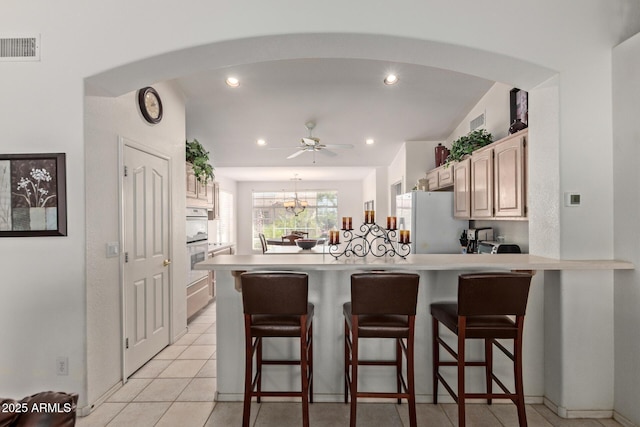 kitchen with freestanding refrigerator, arched walkways, a peninsula, a breakfast bar area, and recessed lighting