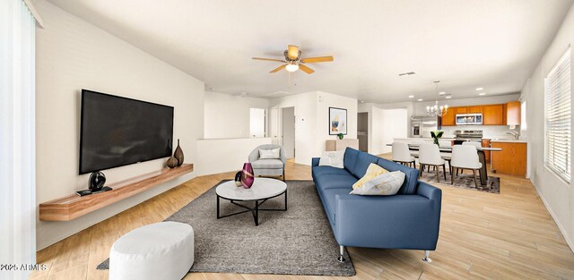 living room featuring ceiling fan with notable chandelier and light wood-type flooring