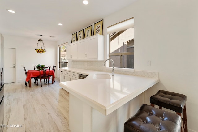 kitchen featuring a kitchen bar, kitchen peninsula, hanging light fixtures, white cabinets, and light hardwood / wood-style flooring