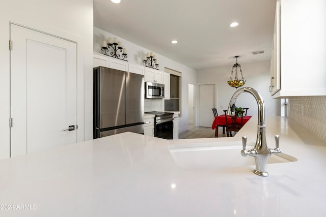 kitchen featuring kitchen peninsula, sink, white cabinetry, appliances with stainless steel finishes, and tasteful backsplash