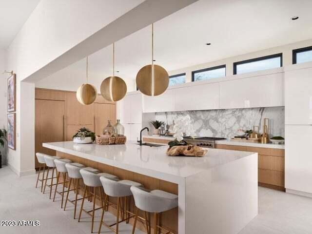 kitchen with a kitchen island with sink, white cabinets, sink, hanging light fixtures, and tasteful backsplash