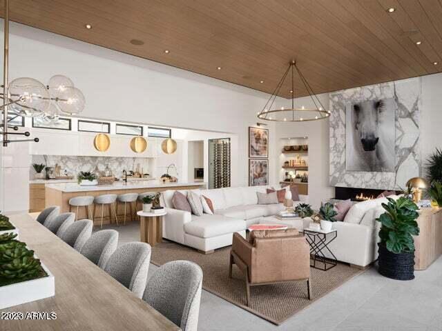 living room with a premium fireplace, a towering ceiling, wooden ceiling, and an inviting chandelier