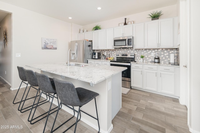 kitchen featuring appliances with stainless steel finishes, a kitchen breakfast bar, tasteful backsplash, a kitchen island with sink, and white cabinets