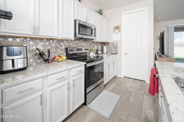 kitchen featuring white cabinets, appliances with stainless steel finishes, decorative backsplash, and light stone countertops