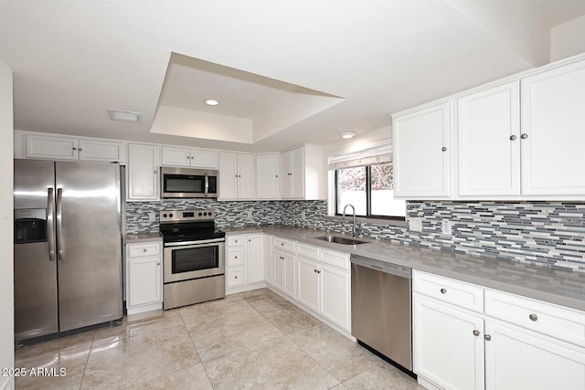 kitchen with white cabinets, sink, a tray ceiling, tasteful backsplash, and stainless steel appliances