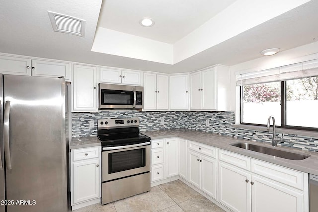 kitchen featuring white cabinets, a raised ceiling, sink, light tile patterned floors, and stainless steel appliances