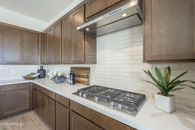 kitchen featuring light wood finished floors, tasteful backsplash, extractor fan, light stone countertops, and stainless steel gas stovetop