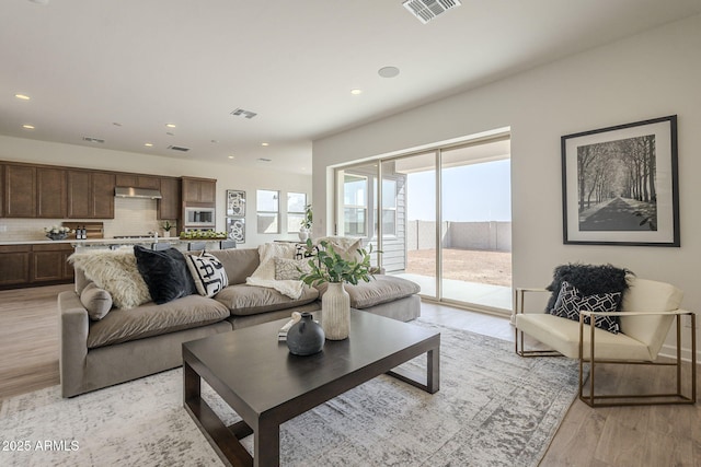 living area with light wood finished floors, visible vents, and recessed lighting