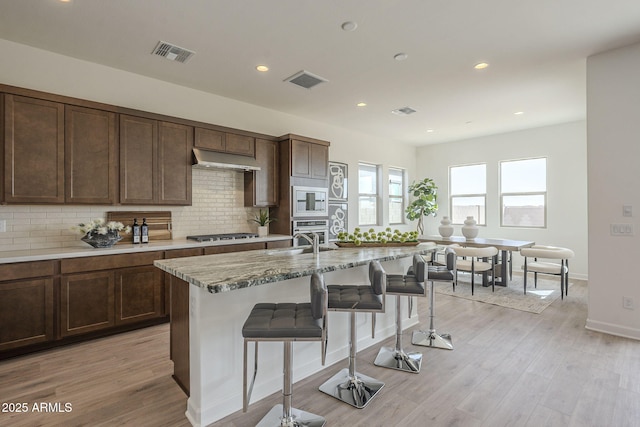 kitchen featuring under cabinet range hood, built in microwave, visible vents, and a breakfast bar