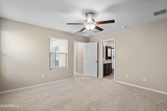 unfurnished bedroom with ceiling fan, ensuite bathroom, and light carpet