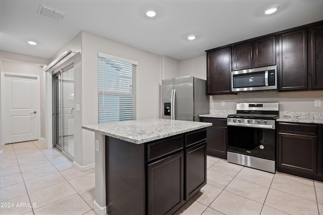 kitchen with a kitchen island, appliances with stainless steel finishes, light tile patterned floors, dark brown cabinetry, and light stone countertops